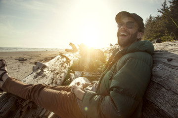 Fototapeta premium Man sitting on log at beach in sunlight