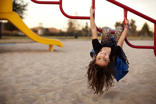 Portrait of girl hanging upside down on monkey bars at park