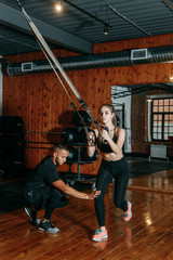 Naklejka na ściany i meble Sports couple engaged in the gym. Training with a trainer, helps and controls. Beautiful girl is engaged in sports