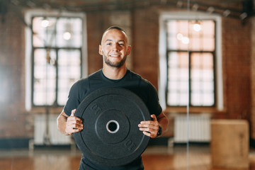 The young man is engaged in the gym, barbell, dumbbells and kettlebells in his hands. Smiling and...