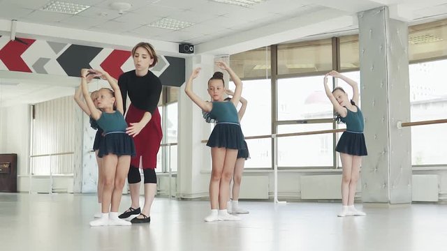 A ballet teacher teaches little ballerinas in a ballet class. teacher corrects student