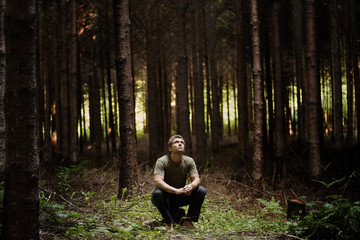 Fototapeta premium Man sitting on tree stump in forest and looking up