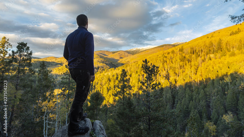 Wall mural man standing on a big rock outcrop overlooking a beautiful forest in fall colors