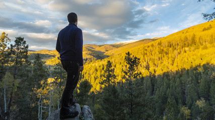 Obraz premium mężczyzna stojący na dużej wychodni skalnej z widokiem na piękny las w jesiennych kolorach