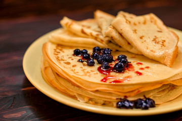 Delicious pancakes with berries and sweet syrup on a dark background