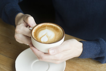 A cup of coffee with milk in the hands.