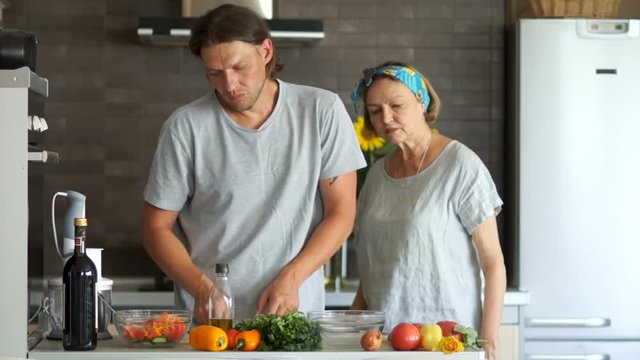 Happy mother and her adult son talking to each other in the kitchen while preparing food. Man in the kitchen, cut salad, Mother's Day