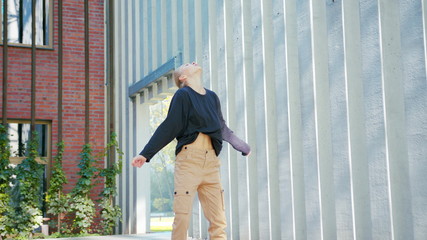 A young girl performs modern hip hop dance on the streets of the city during the summer, twisting and rotating.