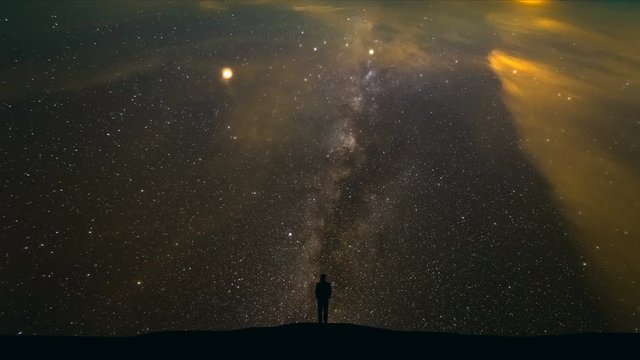 The man standing on a mountain on the starry sky background. time lapse