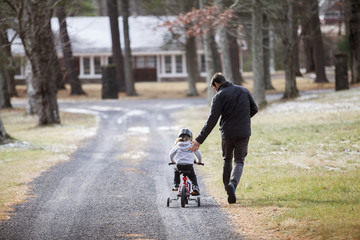 Fototapeta premium Rear view of father assisting boy riding bicycle