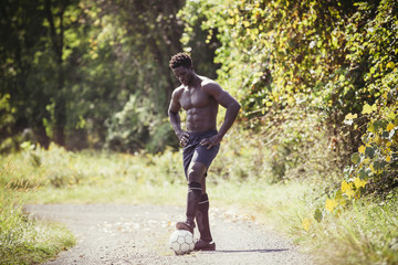 Fototapeta premium Shirtless young man playing with soccer ball on dirt road during sunny day