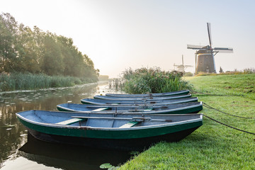 Three wind mills of Molendriegang Leidschendam, Netherlands during a misty Sunrise with five rowing boats in the foreground © Emma