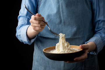 Woman in blue apron holding bowl with stracciatella mozzarella cheese on dark background