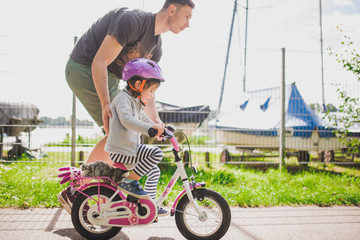 father teaches little toddler daughter to ride a bike in the park