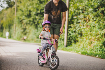 father teaches little toddler daughter to ride a bike in the park