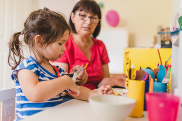 Obraz na płótnie Canvas granddaughter doing handycraft together with her grandmother in nursery, improvement of fine motor skills