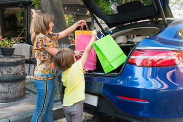 Mother and the daughter put bags in a car luggage carrier.