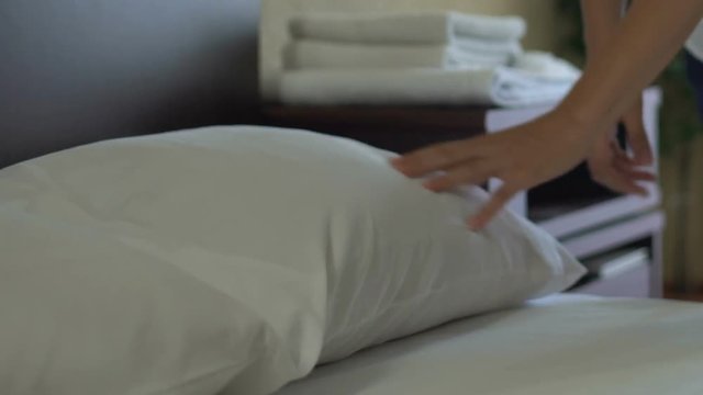 Maid making bed and adjusting pillows in five star hotel, impeccable service