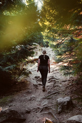 Fototapeta premium Back view of a blonde girl hiking in a dark moody mountain path in a mysterious nature pine forest. Brocken, nature reserve Harz mountains, National Park Harz in Saxony-Anhalt, Germany