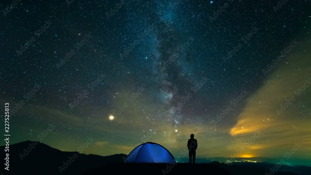 Wall mural the man near camping tent standing on a meteor shower background. time lapse
