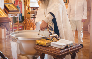 Christening ceremony in the Orthodox church, priest lighting candles at children baptismal font, close up