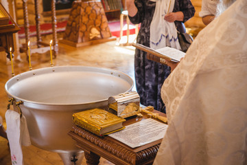Christening ceremony in the Orthodox church, priest lighting candles at children baptismal font,...