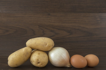 Fototapeta na wymiar potatoes, onion and egg on brown background