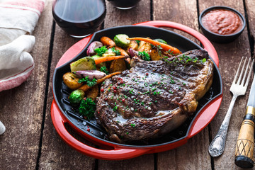 Juicy beef steak close view on iron cast pan with root vegetables