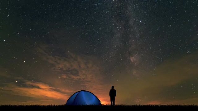 The man near a camping tent standing on stars background. time lapse