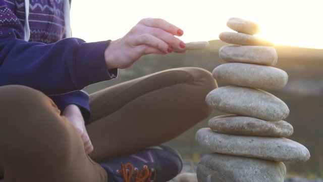Girl collects a pyramid of stones close up at sunset,slow mo