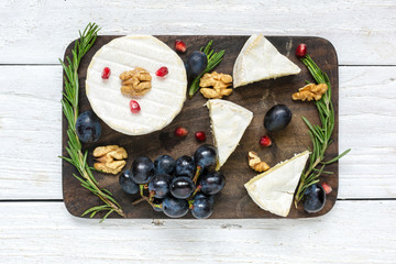 camembert cheese with grapes, pomegranate seeds, walnuts and rosemary on wooden cutting board © samael334