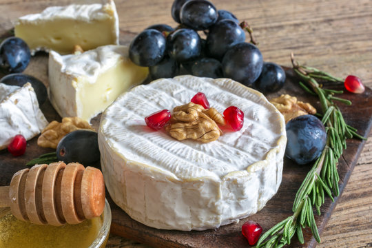 camembert cheese with grapes, pomegranate seeds, honey walnuts and rosemary on wooden cutting board.