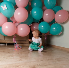 Fototapeta na wymiar little girl sitting on the floor in the room next to the balloons, first birthday, celebrate. one year old blue and pink balls with butterflies. girl in white and blue dress