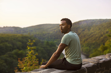 Fototapeta premium Pensive man sitting on wall and looking at landscape