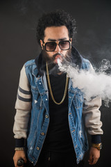 Vaping man holding a mod. A cloud of vapor. Black background. Vaping an electronic cigarette with a...