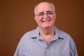 Fototapeta premium Overweight senior man wearing eyeglasses against brown backgroun
