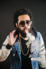 Vaping man holding a mod. A cloud of vapor. Black background. Vaping an electronic cigarette with a...