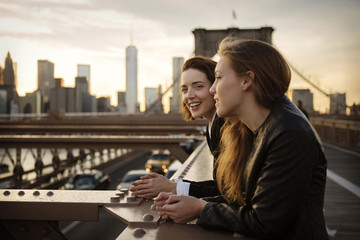Two women talking while standing by railing at Brooklyn Bridge, NYC, USA