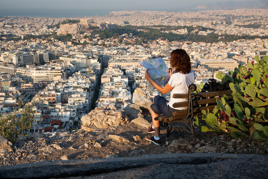 woman with a map sitting on Lycabettus Hill, the highest point in the city overlooking Athens with the Acropolis - world traveller