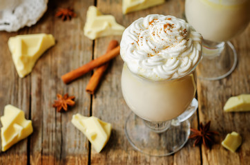 Hot white chocolate with whipped cream and cinnamon on a wood background