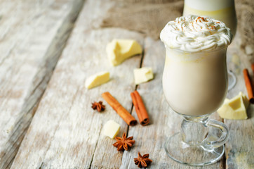 Hot white chocolate with whipped cream and cinnamon on a wood background
