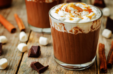 Dark hot chocolate with whipped cream and salted caramel sauce on a wood background