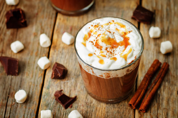 Dark hot chocolate with whipped cream and salted caramel sauce on a wood background