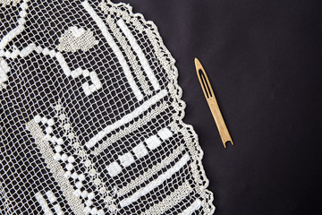 Close up view of ancient hand knotted net darned filet lace with old wooden netting tool needle on against black background.