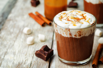 Dark hot chocolate with whipped cream and salted caramel sauce on a wood background