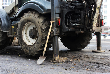 Tractor strong outrigger stabilizing legs extended to stabilize and steady state when digging the soil before applying an asphalt patch on a part of the road during repair