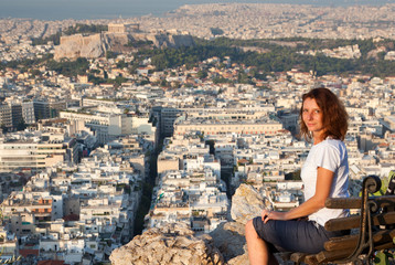 woman sitting on Lycabettus Hill, the highest point in the city overlooking Athens with the Acropolis - world traveller