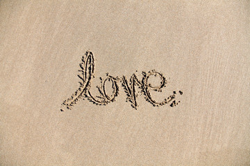 The word 'Love' written in the sand on a beach