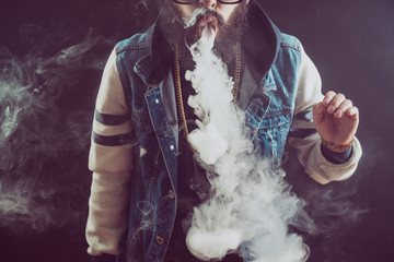 Young man with beard throwing a cloud of steam. Black background. Vaping an electronic cigarette...