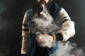 Young man with beard throwing a cloud of steam. Black background. Vaping an electronic cigarette...